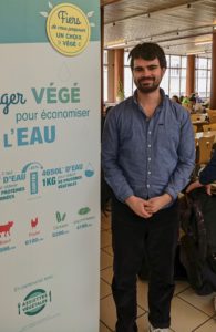 Keyvan, chargé de végétalisation pour Assiettes Végétales, pose devant une affiche sur les économies de ressources en eau
