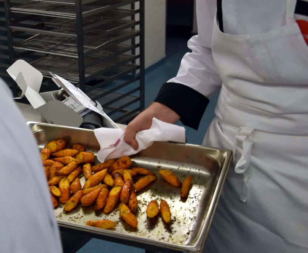 Un chef tend un plat de carottes rôties